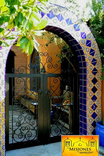 arched double door courtyard gate with black open scroll work set in a mexican tile archway