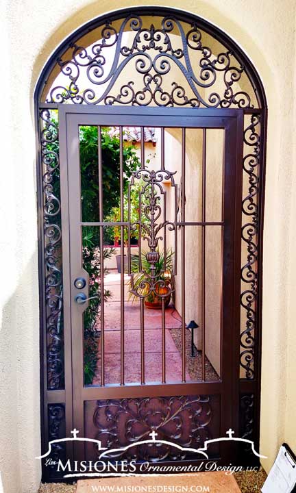 single door ornamental courtyard gate set in an arched frame with a brown finish and decorative kickplate