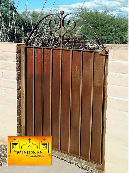 single door short courtyard gate set in a low brick wall, design is simple vertical bars with a rust screen and then topped with symmetrical scrolls