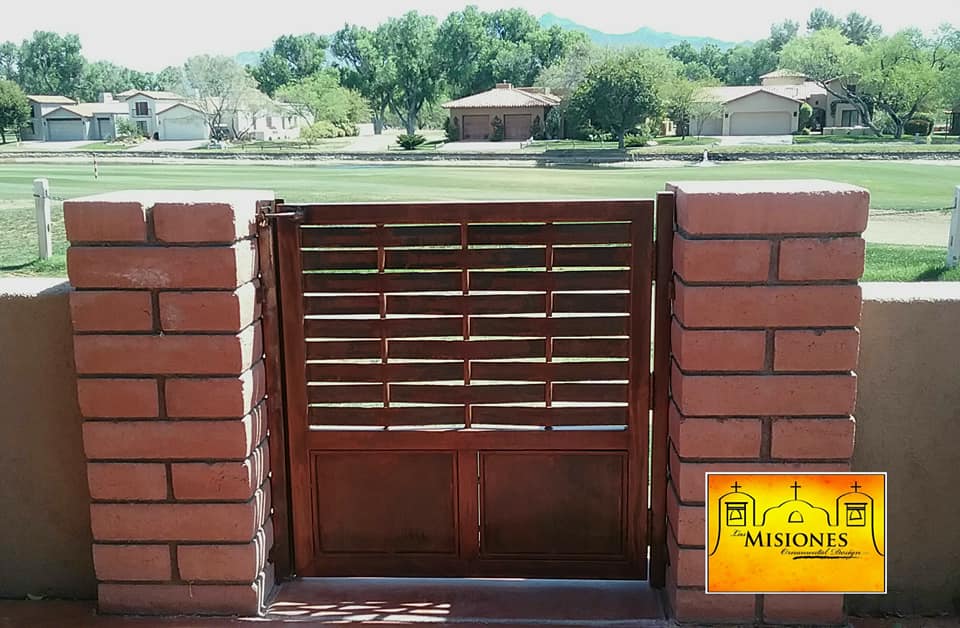 red rust colored, short single door, bottom solid, top has horiztonal woven steel slats, set into brick pillars, steel metal courtyard gate